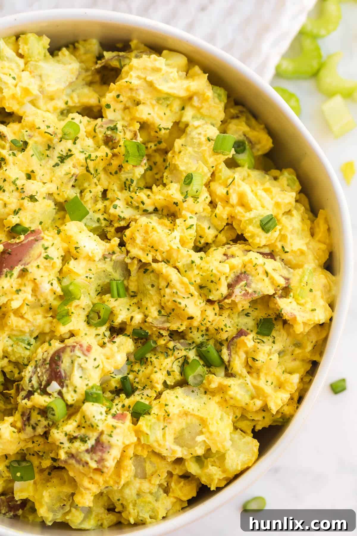 A close-up shot of a single serving of curried potato salad in a small bowl, garnished with a sprig of fresh parsley.
