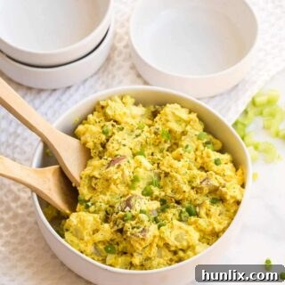 Curried Potato Salad in a bowl with two wooden spoons.