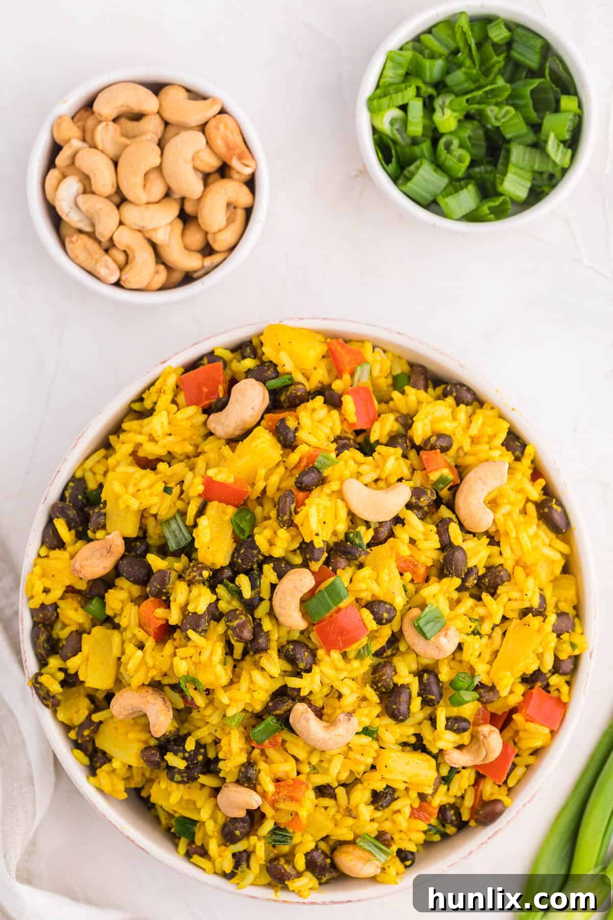 Jamaican Curry Rice 2 A bowl of vibrant Jamaican Curried Rice, garnished with fresh cashews and sliced green onions.