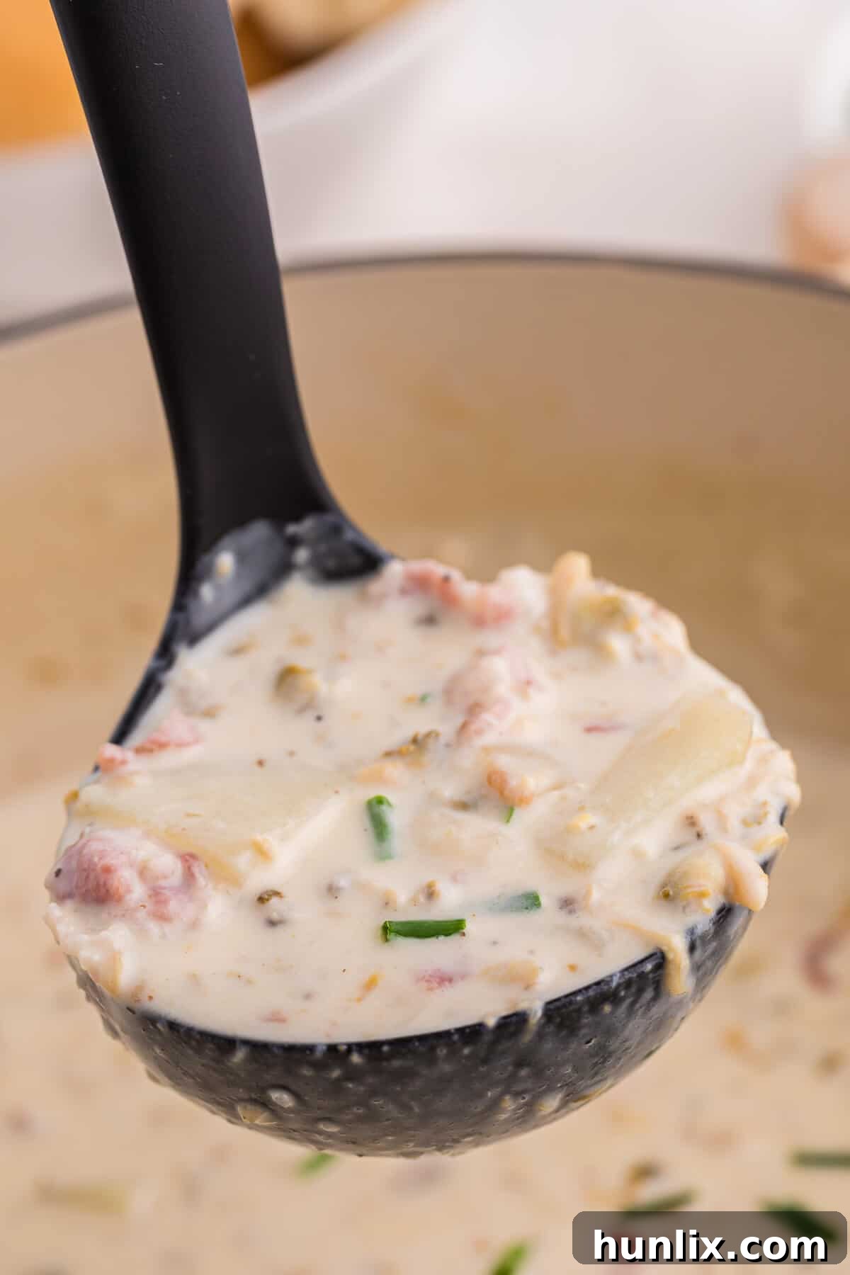 The Quintessential New England Clam Chowder 2 A ladle serving creamy New England Clam Chowder from a large pot, with fresh chives as garnish.