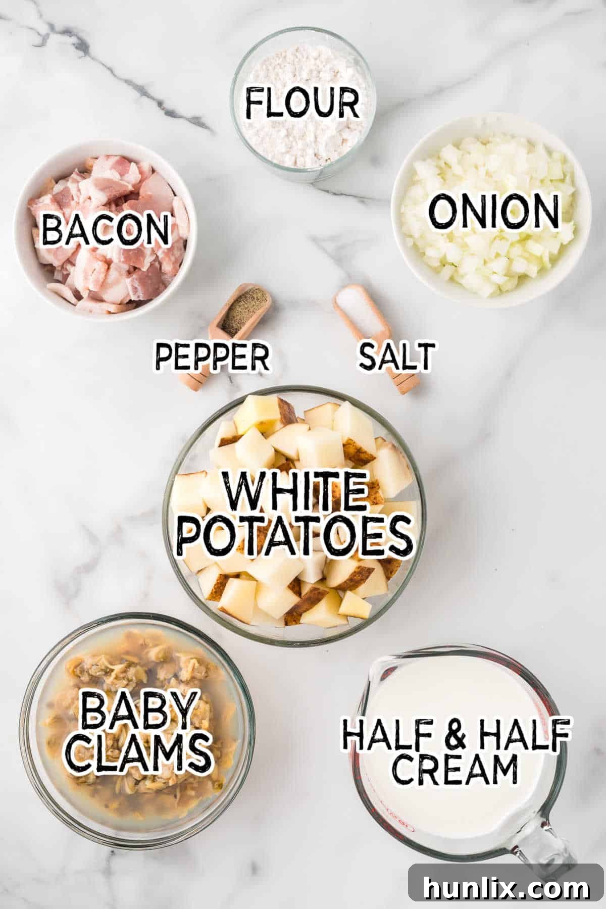 The Quintessential New England Clam Chowder 3 A flat lay image displaying all the raw ingredients needed for making New England Clam Chowder: chopped bacon, diced yellow onion, flour, unpeeled chopped white potatoes, cans of baby clams, salt, pepper, and half & half cream.