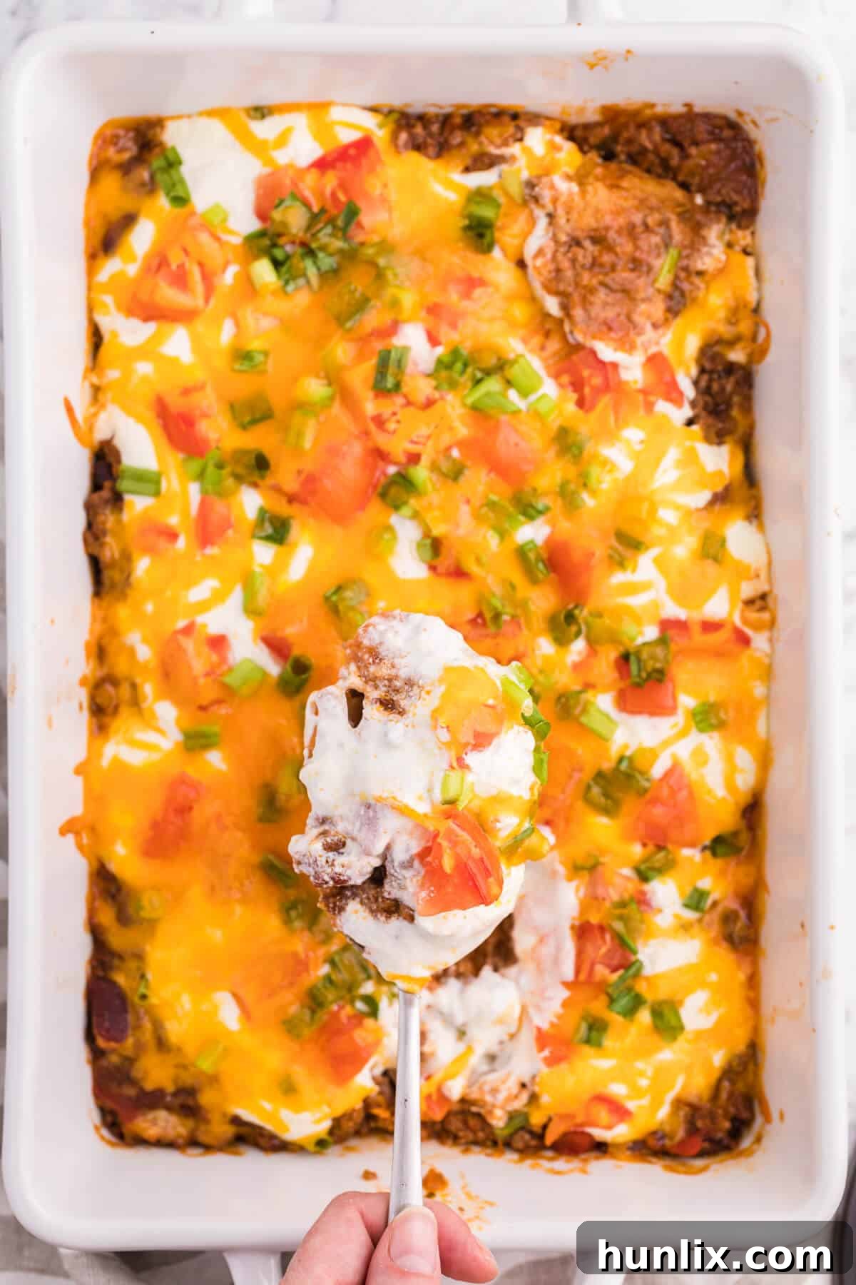 A serving spoon over a pan of taco casserole, showing the cheesy top.