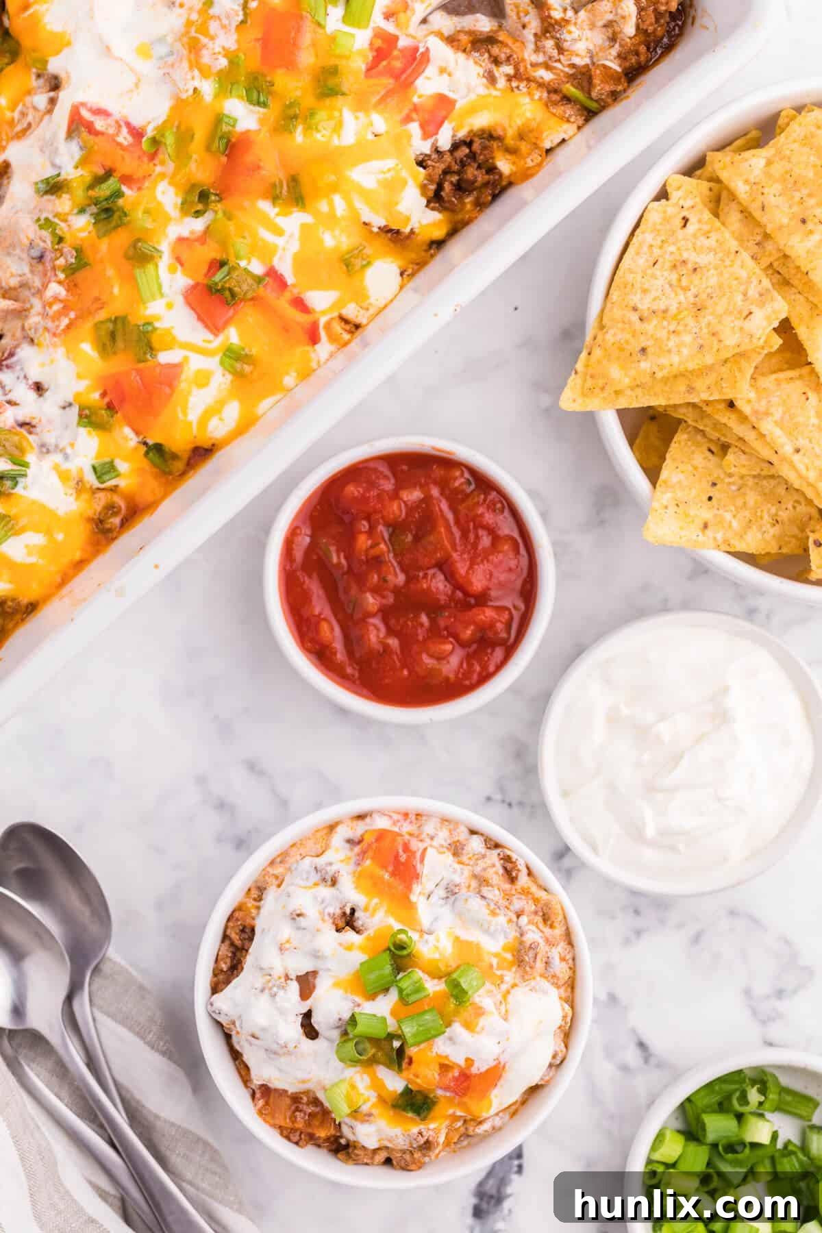 A bowl of taco casserole with various toppings around it, inviting customization.