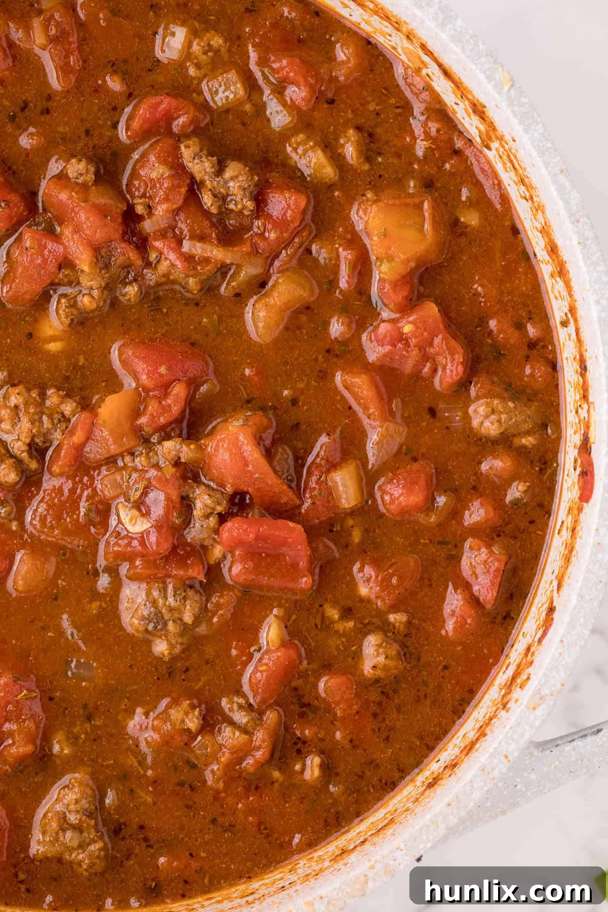 A large white Dutch oven filled with simmering taco soup, garnished with melted cheese.