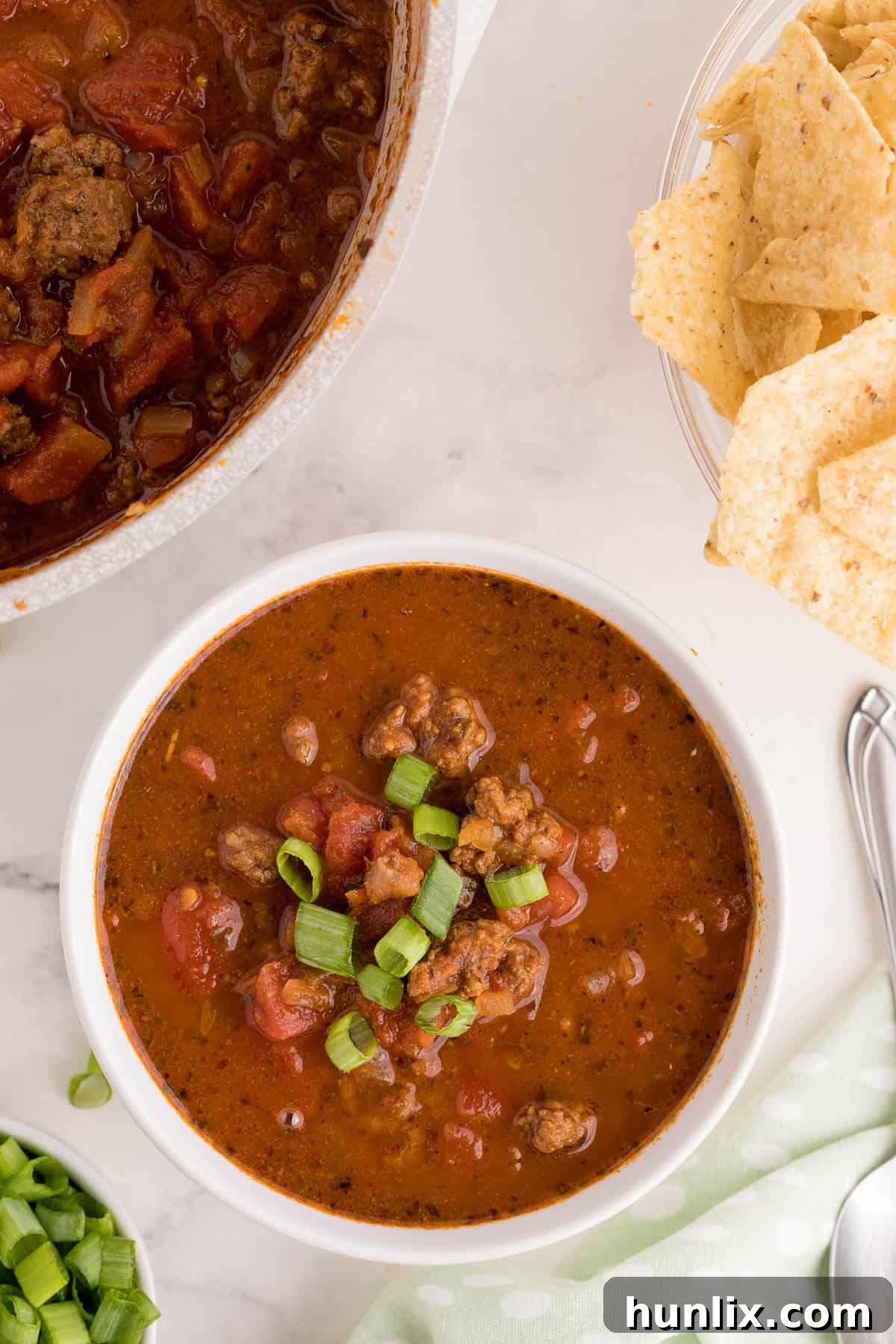 A single serving of taco soup in a white bowl, garnished with fresh cilantro and cheese, placed on a white surface.