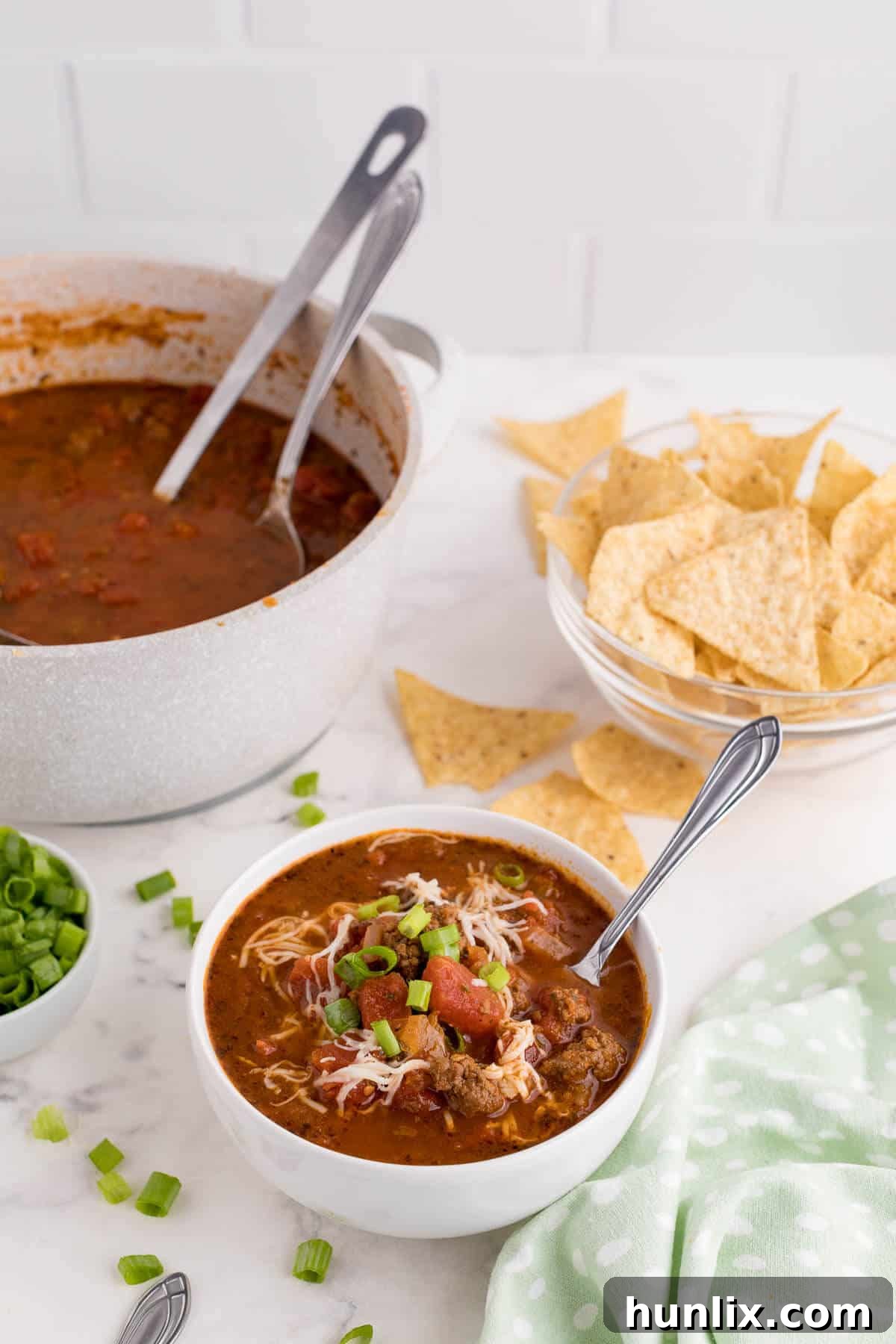 A bowl of rich taco soup, garnished with a swirl of sour cream and fresh herbs, presented on a white wooden surface.