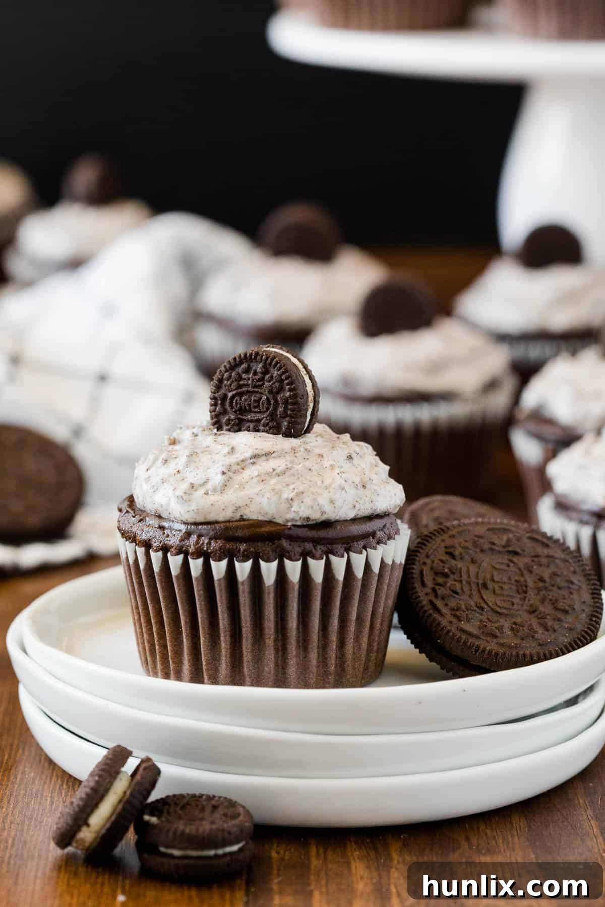 A single Oreo cupcake on a white plate, served next to a whole Oreo cookie, highlighting its deliciousness.
