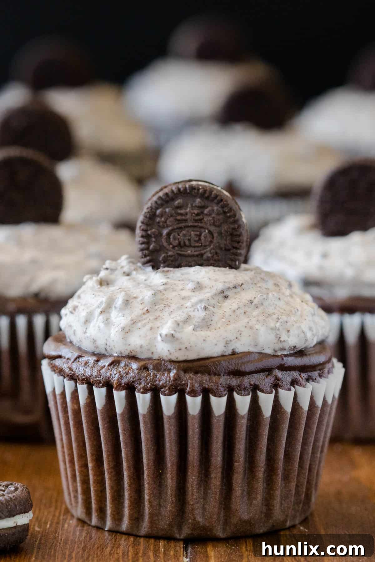 A single Oreo cupcake resting on a rustic wooden surface, highlighting its texture and inviting appearance.