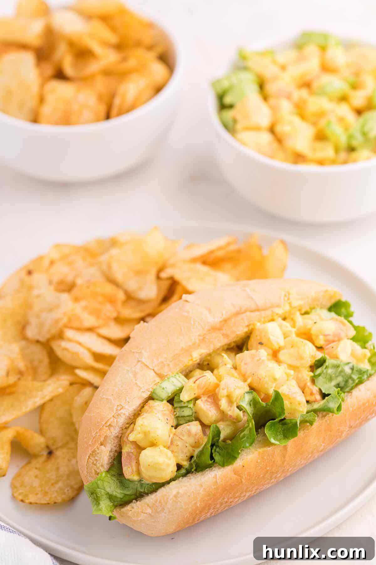 Close-up of a Curried Shrimp Roll on a plate, surrounded by golden potato chips, highlighting its creamy texture.