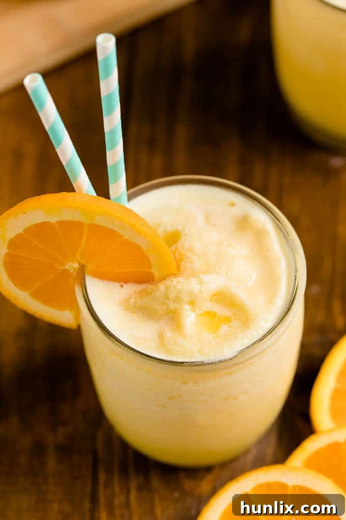 The Orange Julius recipe in a glass cup with straws and an orange slice.