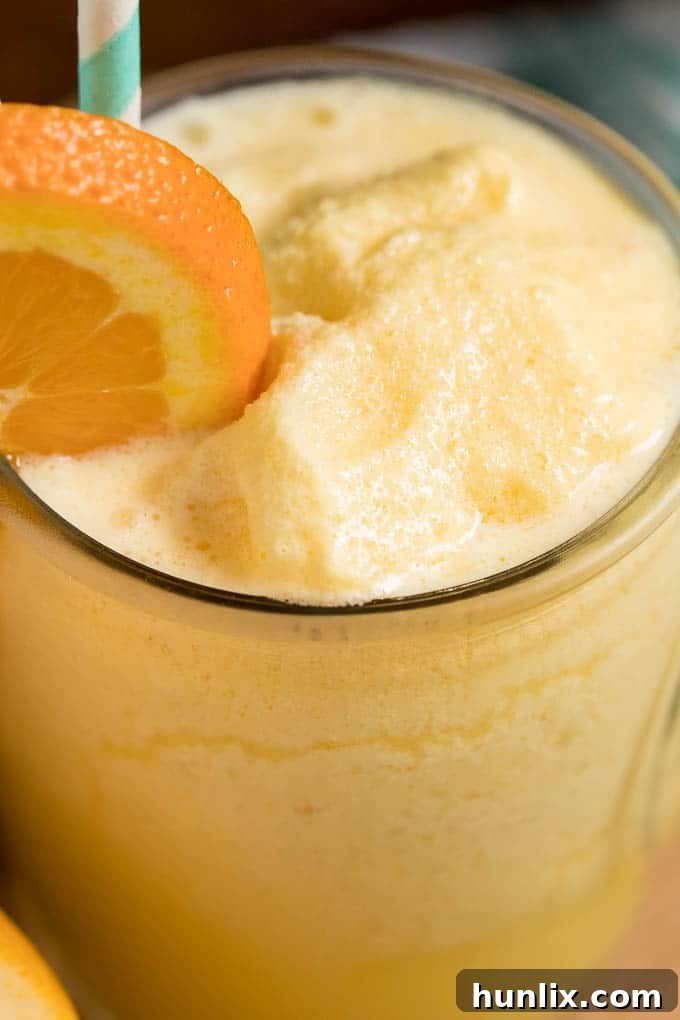 The Orange Julius recipe in a glass cup with straws and an orange slice.