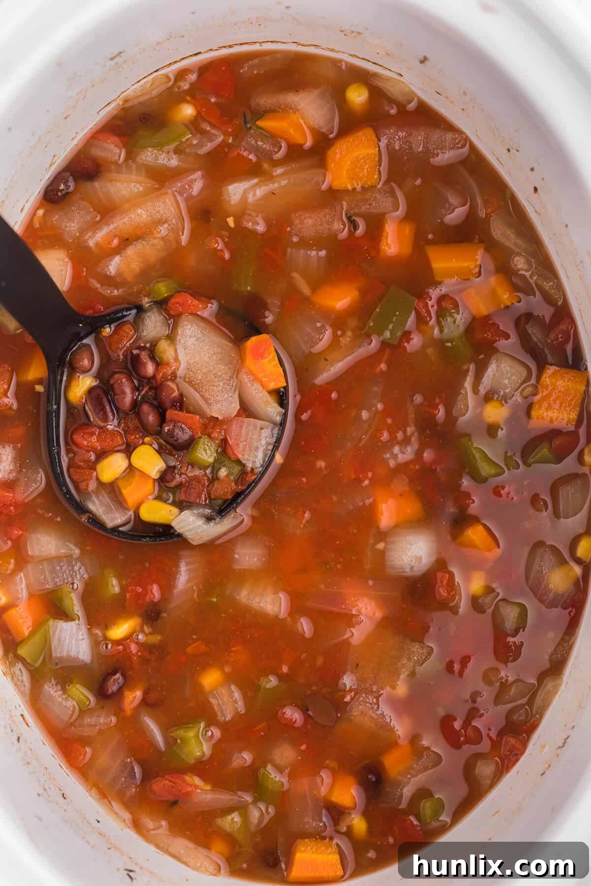 A ladle serving hearty black bean vegetable soup from a slow cooker, brimming with colorful vegetables and savory broth.