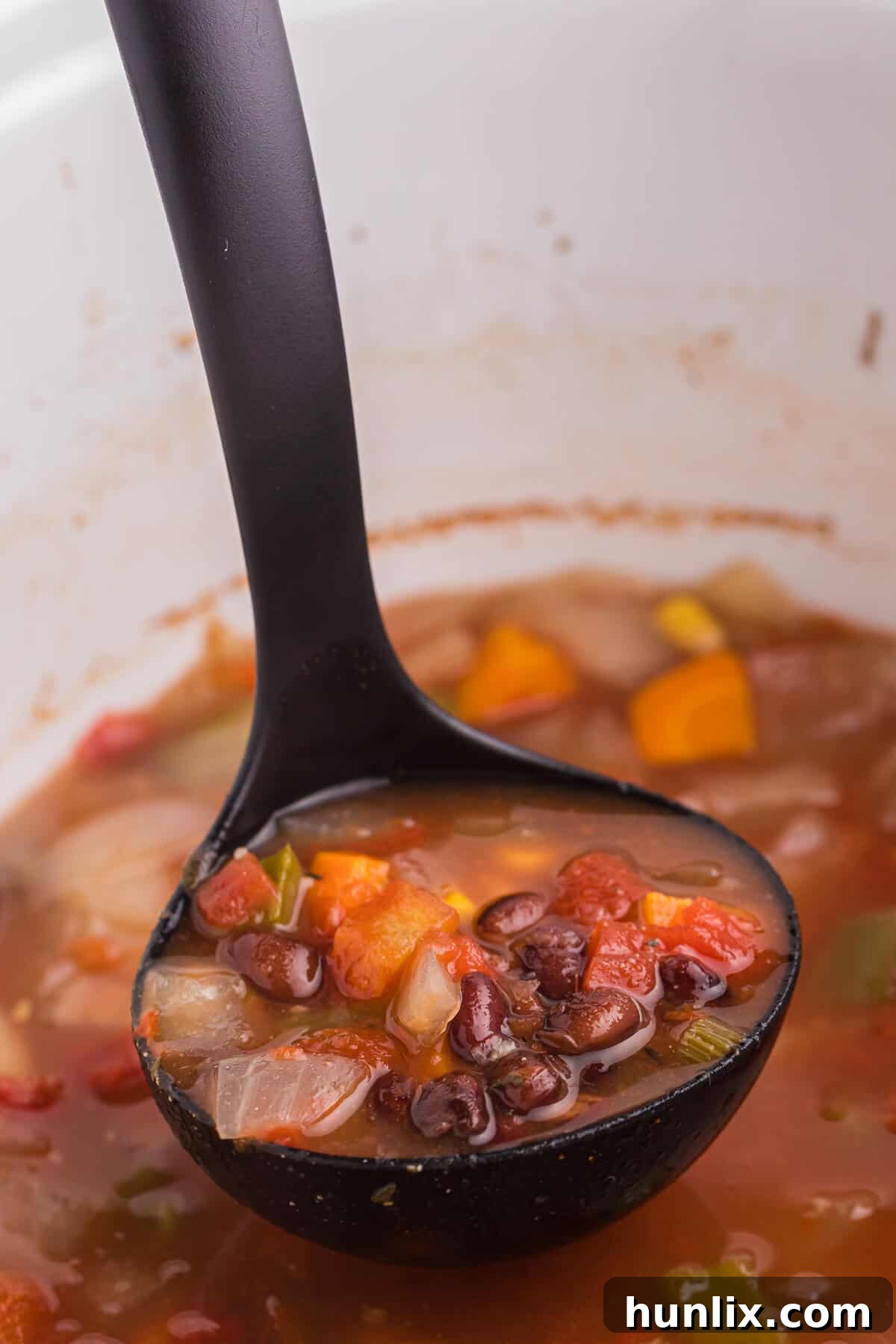 Close-up of vibrant black bean vegetable soup in a bowl, garnished with fresh cilantro and a dollop of sour cream.