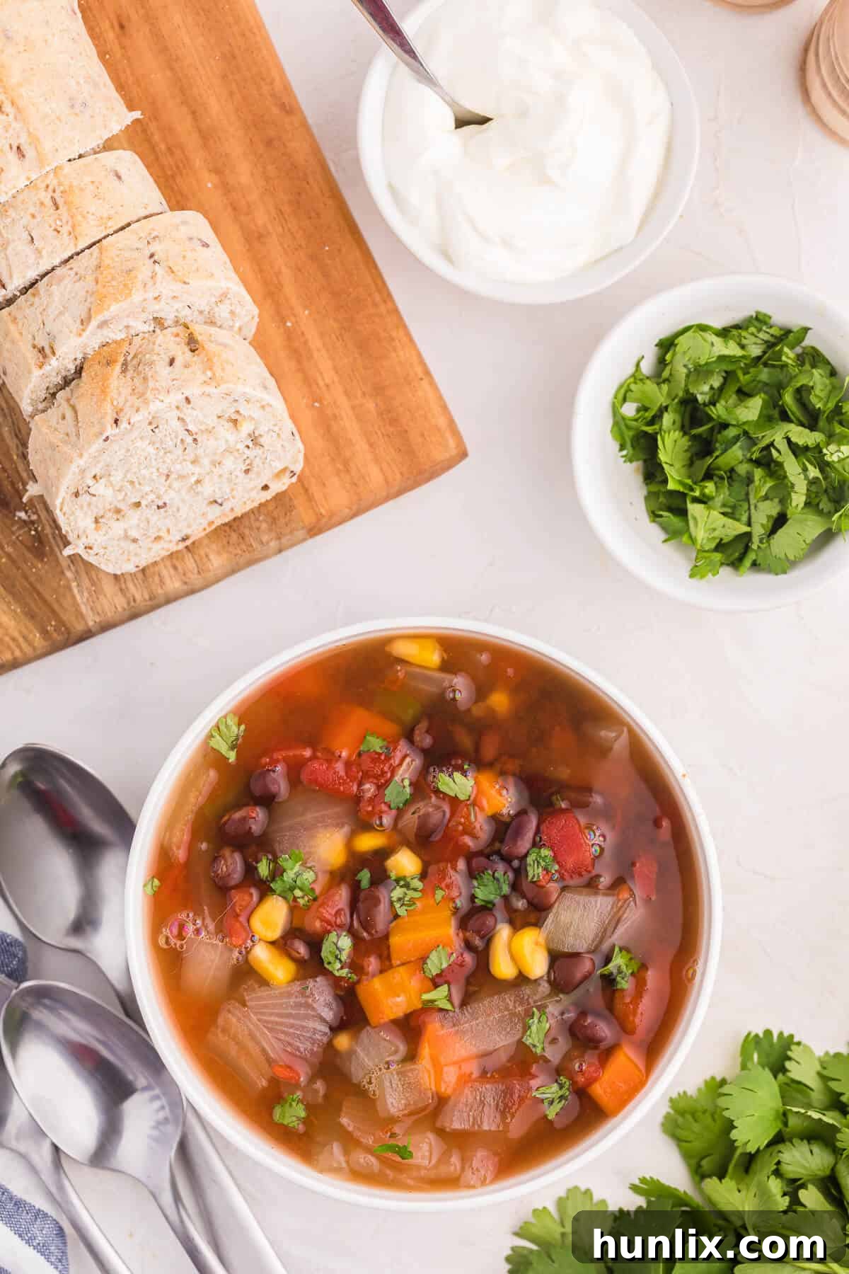 Overhead view of a bowl of Black Bean Vegetable Soup, steaming, with fresh toppings ready to be enjoyed.