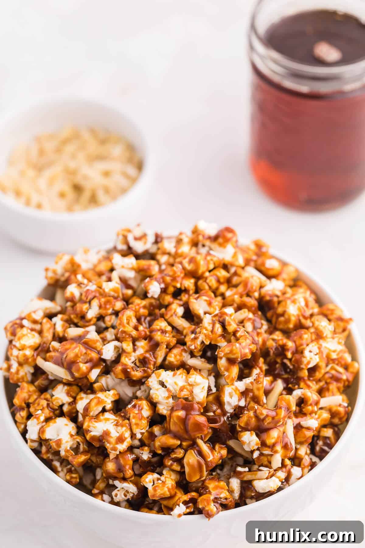 Maple-Glazed Almond Popcorn 3 A close-up view of Maple Almond Popcorn generously placed in a stylish white bowl, emphasizing the inviting texture and glossy maple coating.