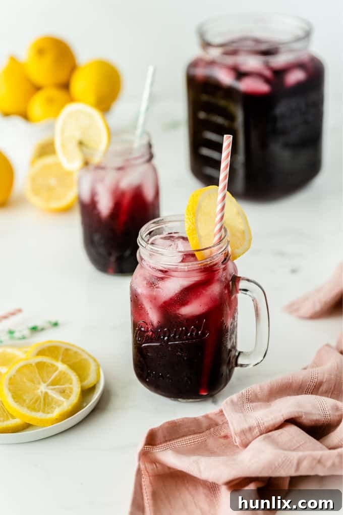 Zesty Grape Lemonade Fizz 3 Several glasses filled with Sparkling Grape Lemonade, garnished with lemon slices, arranged on a pristine white surface, ready to be served.