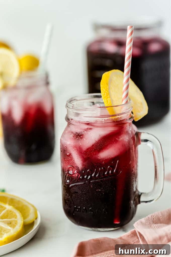 Zesty Grape Lemonade Fizz 4 A single glass of Sparkling Grape Lemonade, beautifully presented with a straw and a fresh lemon slice garnish, ready to be enjoyed.