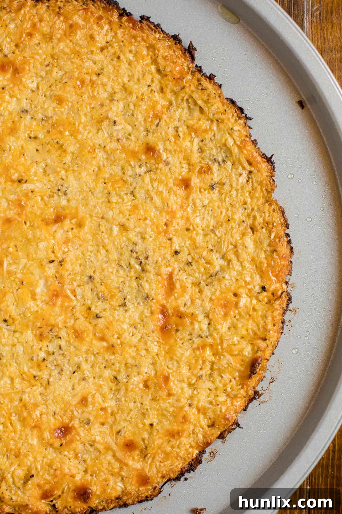 A freshly baked cauliflower pizza crust on a pizza pan, brushed with olive oil and ready for sauce and toppings.