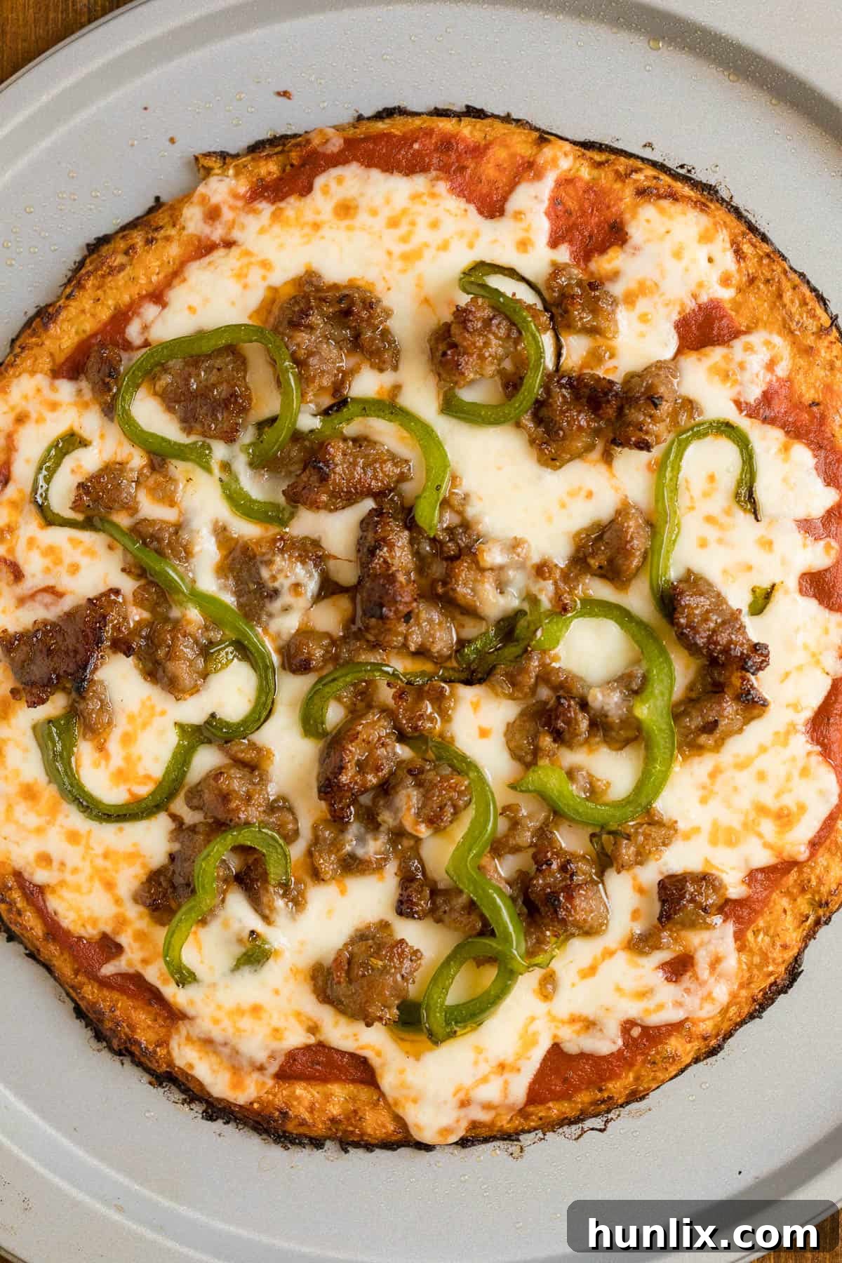 A baked sausage pizza made with a cauliflower pizza crust, sliced and ready to serve.