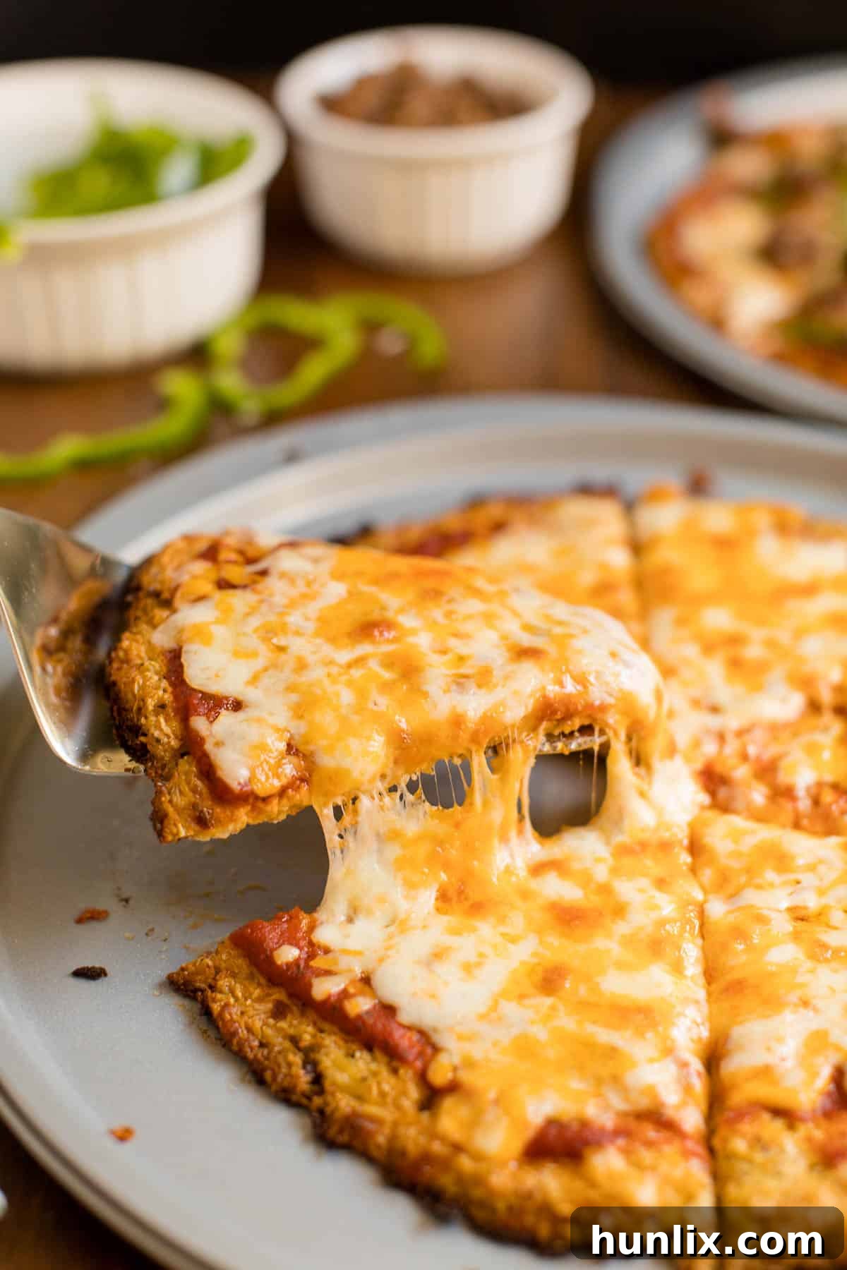 A serving spatula lifting a slice of cheese pizza with a crispy cauliflower crust from a pizza pan.