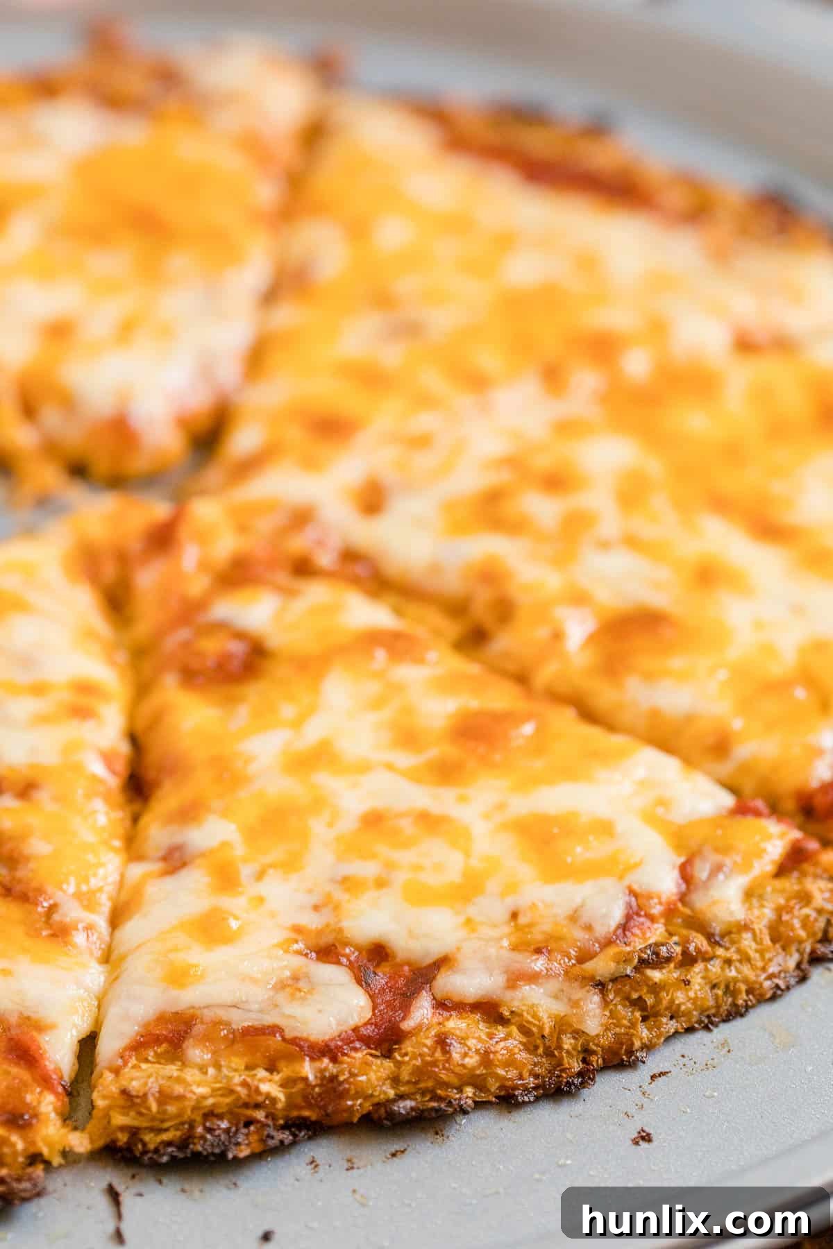 A whole cheese pizza with a golden-brown cauliflower crust on a pizza pan, freshly baked.