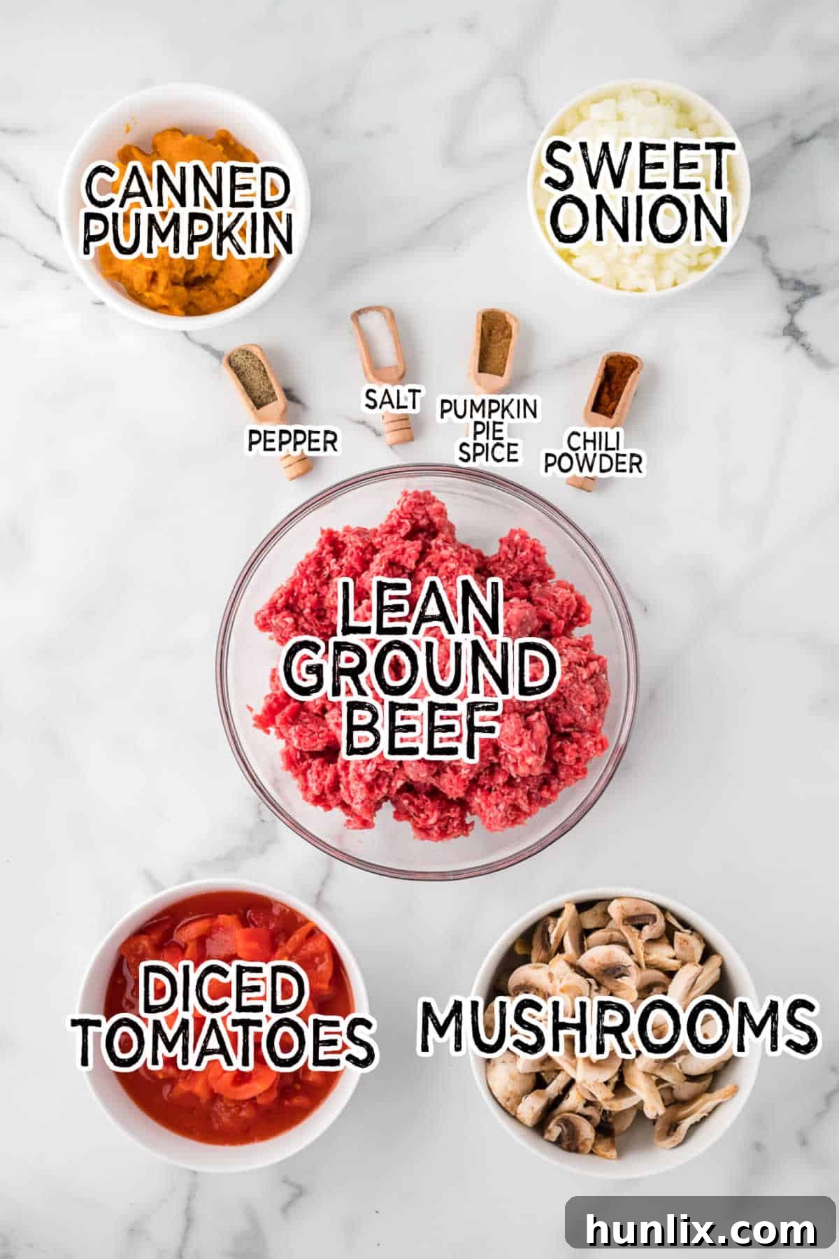 Golden Harvest Pumpkin Chili 3 A selection of fresh ingredients laid out on a white countertop, including ground beef, onions, mushrooms, diced tomatoes, and spices, ready for making pumpkin chili.