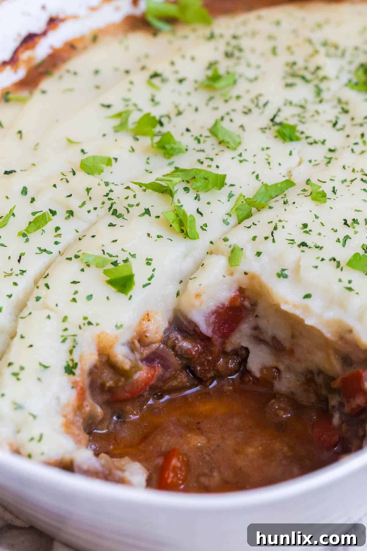 A serving of Beef Picadillo Shepherd's Pie with a piece freshly cut, revealing the savory beef and vegetable filling beneath a creamy cauliflower topping.