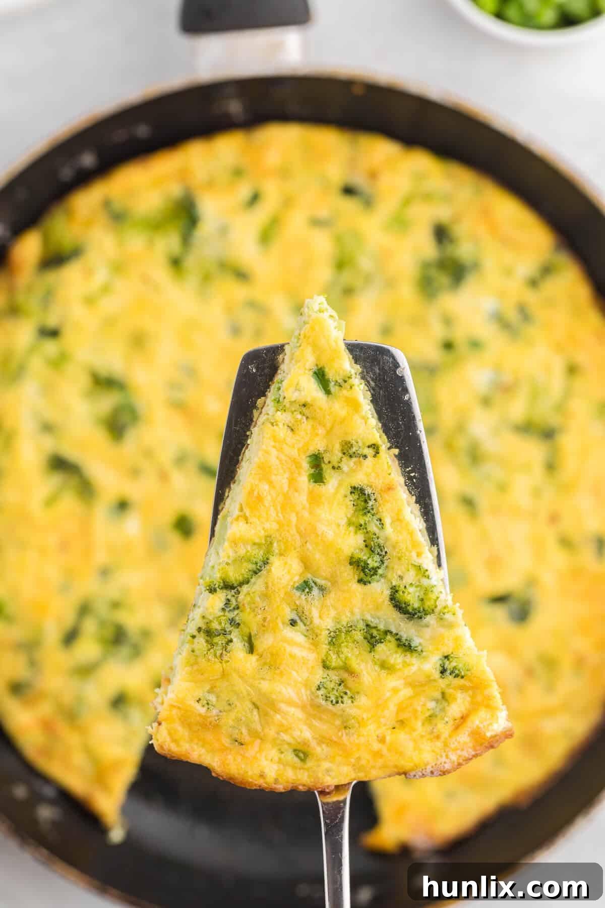 Savory Broccoli Frittata 6 A perfectly cooked slice of broccoli frittata resting on a spatula, showcasing its fluffy interior and golden crust.