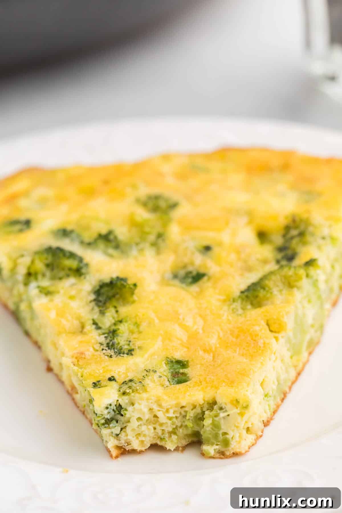 Savory Broccoli Frittata 8 A slice of fluffy broccoli frittata on a white plate, with a fork taking a bite, showing its delicious texture.