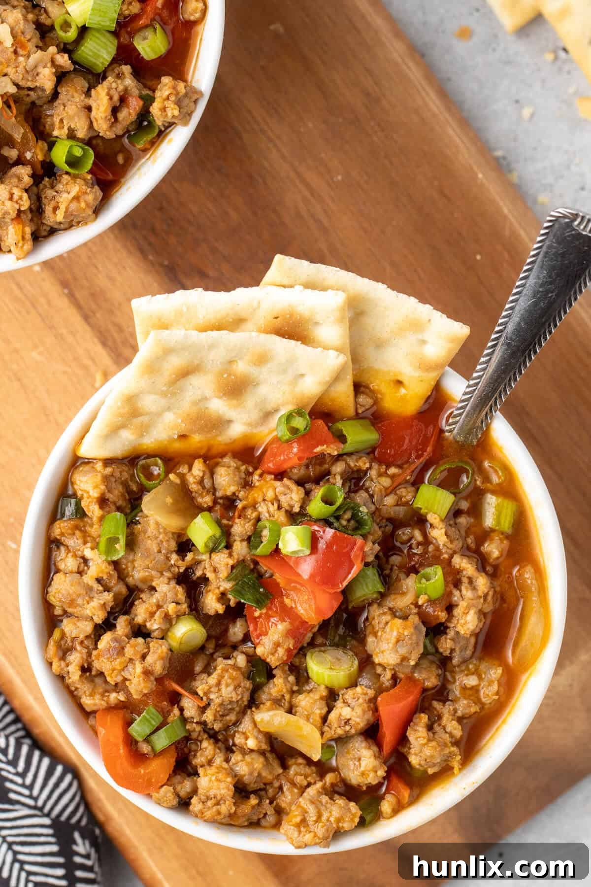 Sizzling Chorizo Stew 8 A bowl of spicy sausage soup with crackers and a spoon, garnished with fresh herbs.