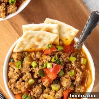 A bowl of spicy sausage soup with crackers and spoon.