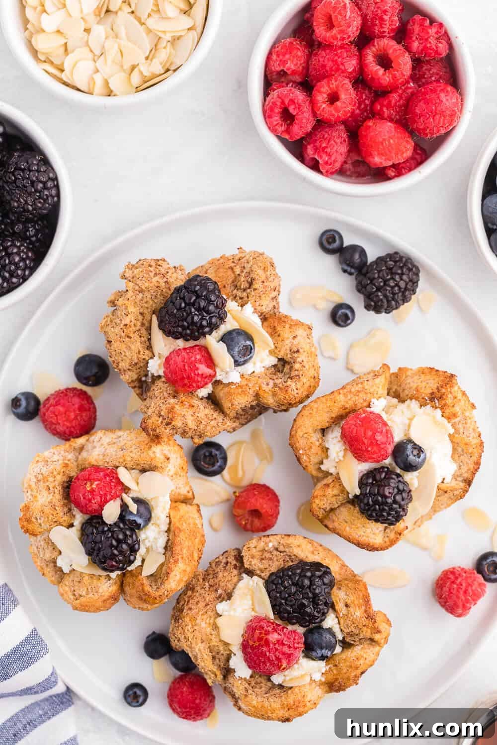 Individual French Toast Cups with ricotta, fresh raspberries, blueberries, and a maple syrup drizzle, served in a white dish on a rustic wooden surface.