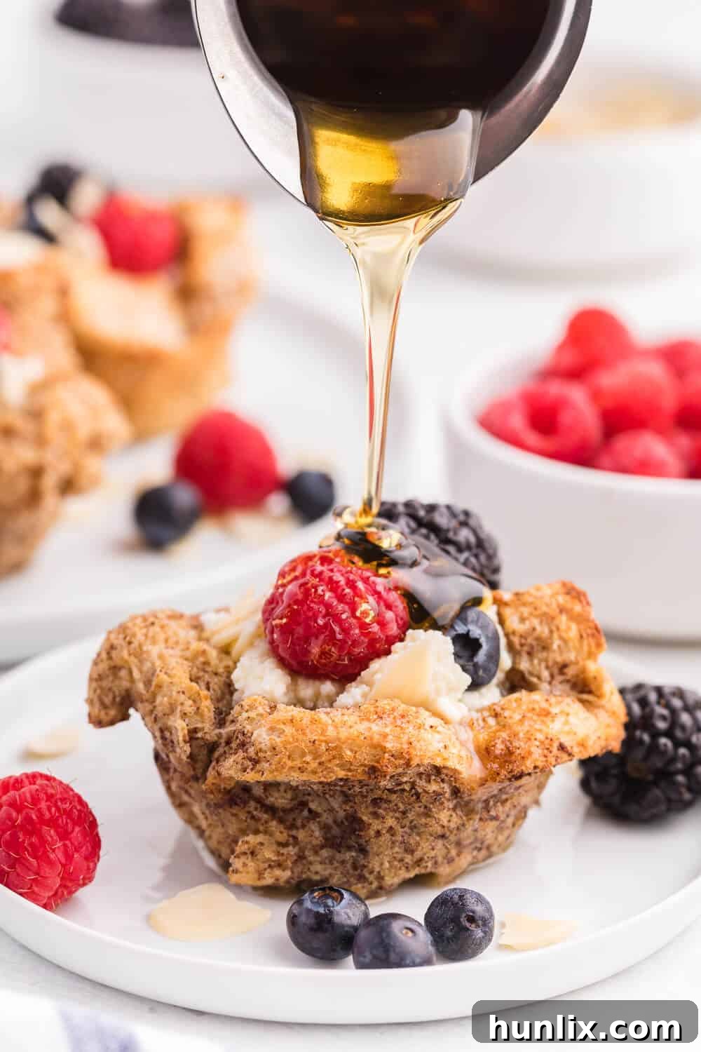 A close-up shot of a single French Toast Cup, beautifully presented with a dollop of ricotta, an array of mixed berries, and glistening with maple syrup.