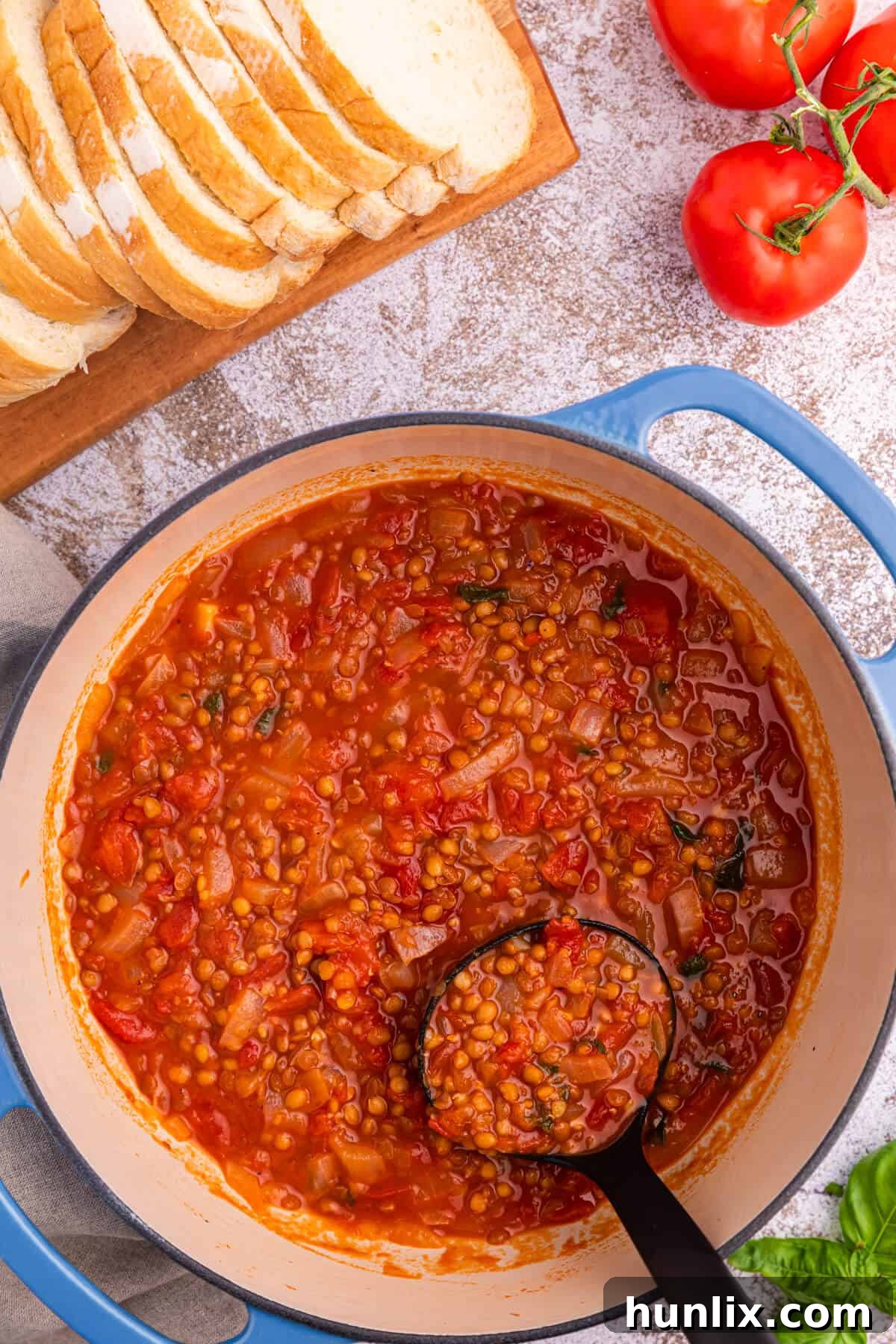 A pot of vibrant tomato lentil soup with a ladle, ready to be served, showcasing its rich texture and inviting color.