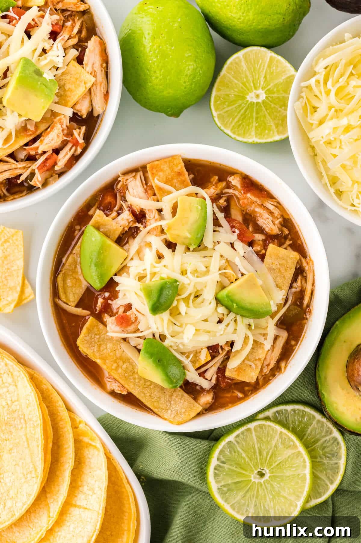 Fiesta Chicken Tortilla Soup 8 A bowl of chicken tortilla soup surrounded by fresh ingredients like lime, avocado, and tortilla chips.