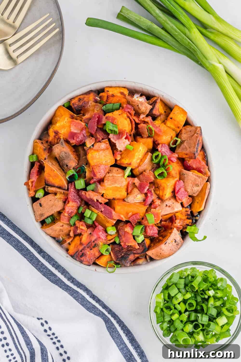 A bowl of sweet potato home fries, garnished with fresh green onions.