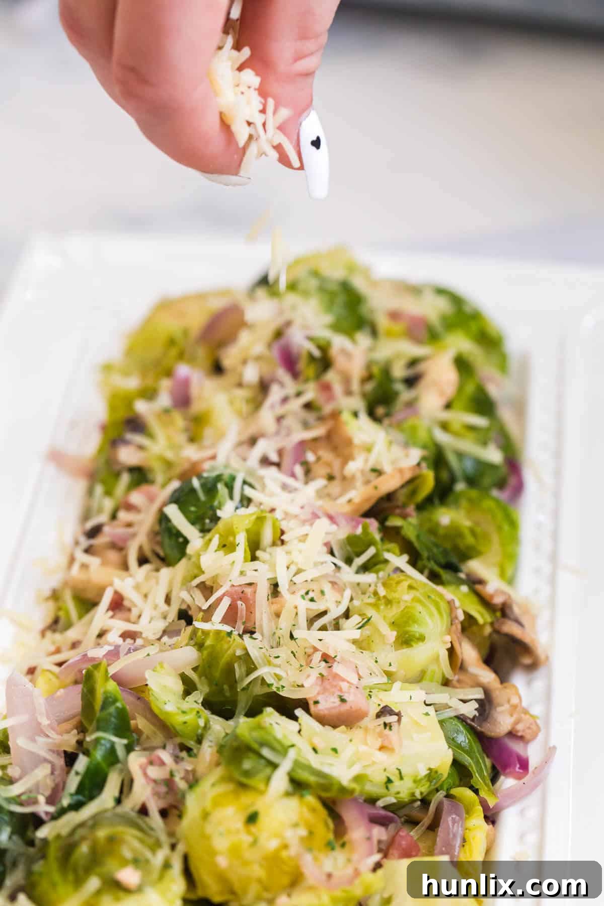 A close-up shot of a hand sprinkling freshly grated Parmesan cheese over a pan of hot Brussels sprouts, creating a delicious finish.