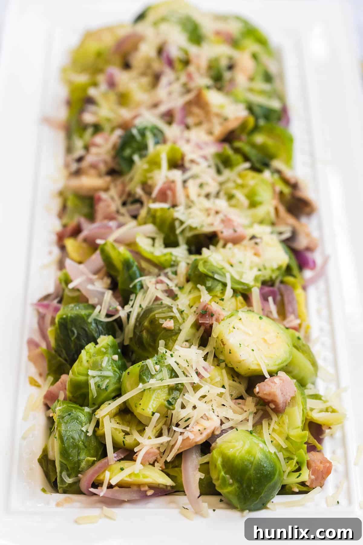 A beautifully presented platter of Brussels sprouts with lemon and pancetta, garnished with fresh herbs, ideal for a family dinner or special occasion.