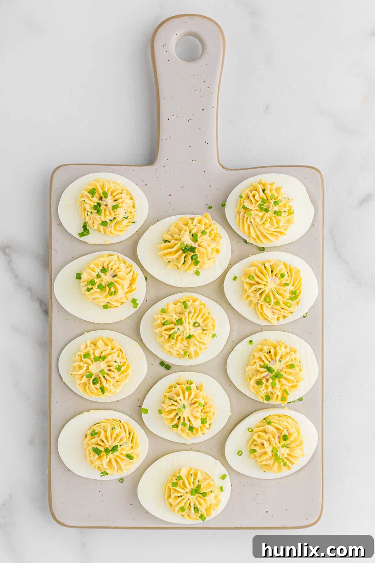 Sinfully Delicious Eggs 2 A serving of Devilish Eggs artfully arranged on a rustic grey cutting board, highlighting their creamy filling and fresh green onion garnish.