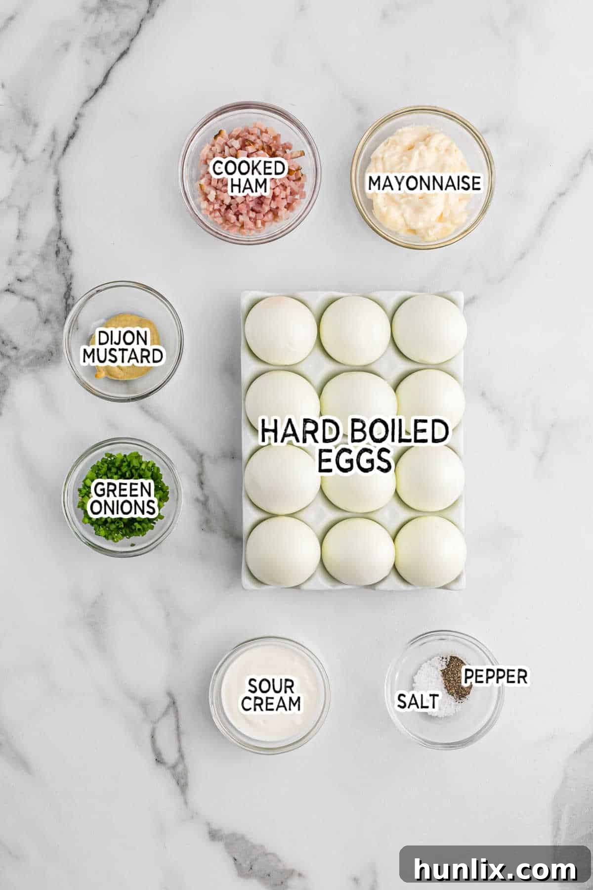 Sinfully Delicious Eggs 3 Ingredients for Devilish Eggs laid out on a clean surface, including hard-boiled eggs, mayonnaise, sour cream, Dijon mustard, cooked ham, and green onions.