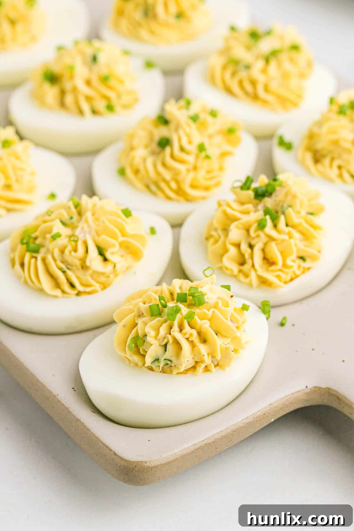 Sinfully Delicious Eggs 6 A close-up shot of Devilish Eggs on a grey cutting board, garnished with finely chopped green onions, ready to be served.