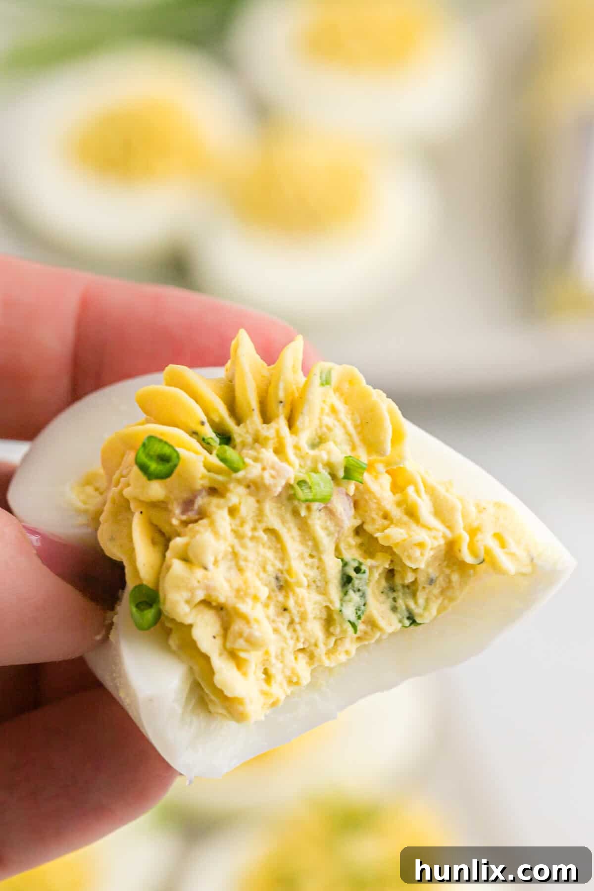 Sinfully Delicious Eggs 8 A hand holding a Devilish egg with a bite taken out, showing the creamy ham and green onion filling.