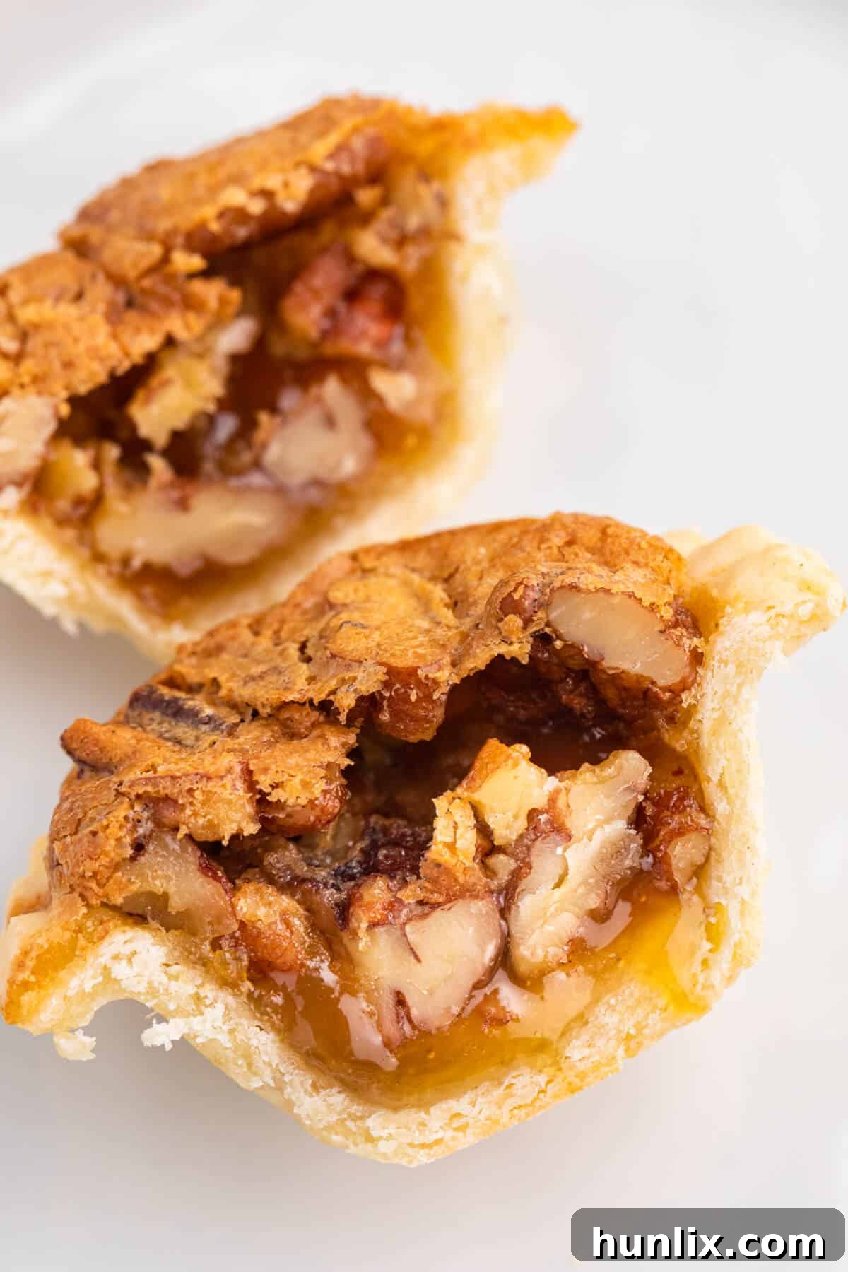 A pecan butter tart, sliced in half to reveal its gooey, nutty filling, served on a plate.