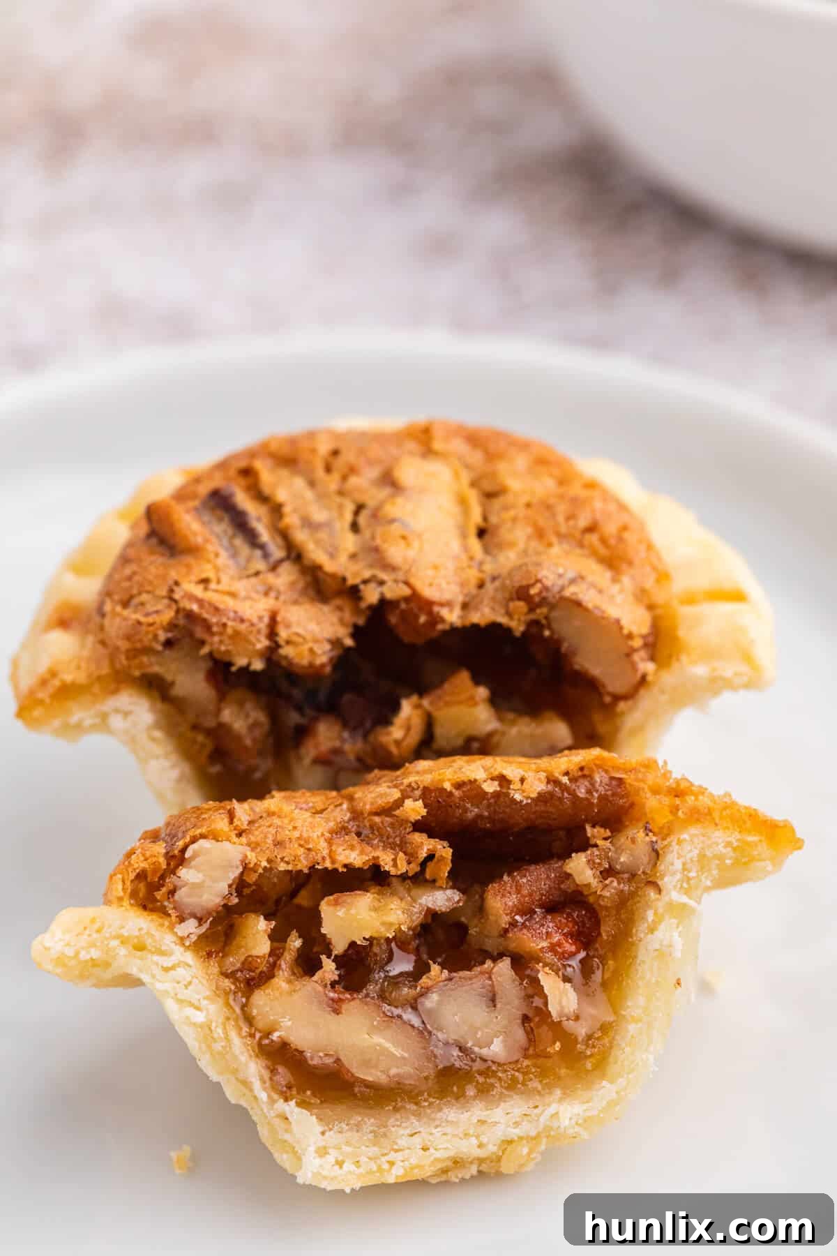 A pecan butter tart, expertly sliced in half, revealing the gooey filling and flaky crust.
