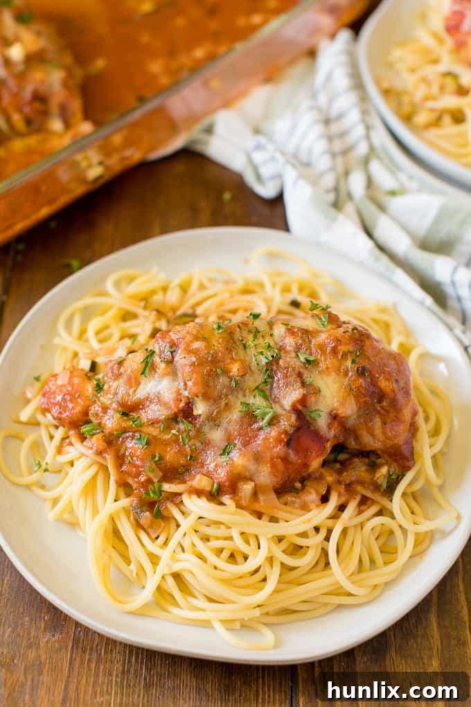 Homestyle Chicken Parmesan Bake 7 Baked Chicken Parmesan served over pasta with a side of fresh parsley garnish.