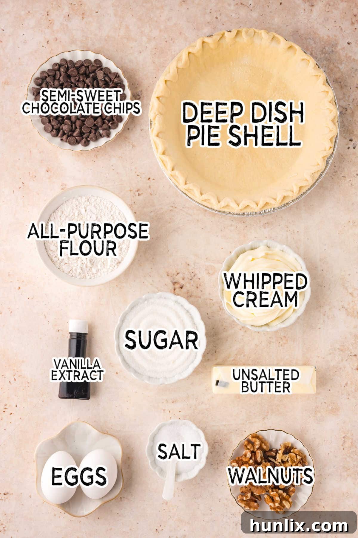 Assorted baking ingredients for brownie pie laid out on a rustic brown wooden surface, including chocolate chips, butter, sugar, vanilla, eggs, flour, and walnuts.