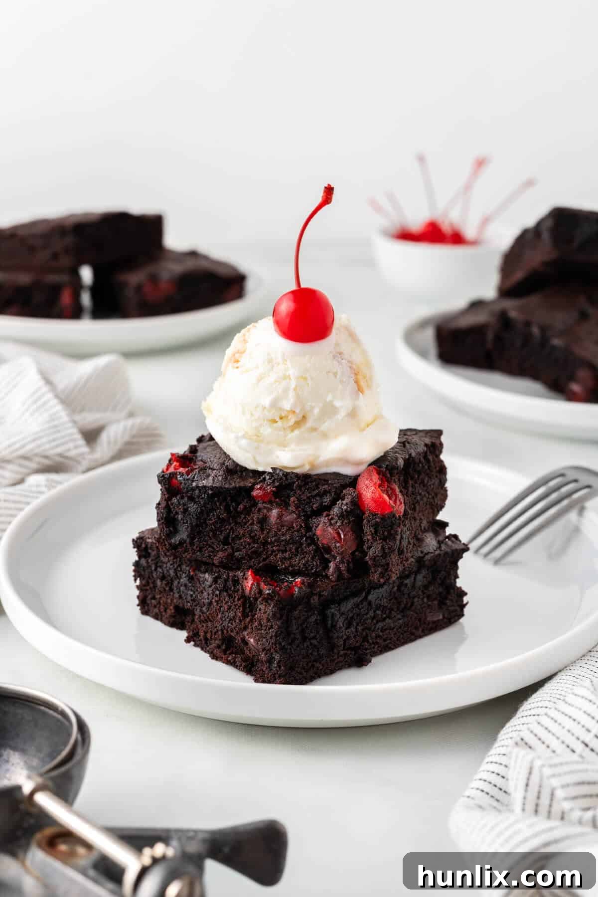 Black Forest Cherry Brownies 12 Two pieces of cherry chocolate brownies stacked on a plate, topped with ice cream and a maraschino cherry.