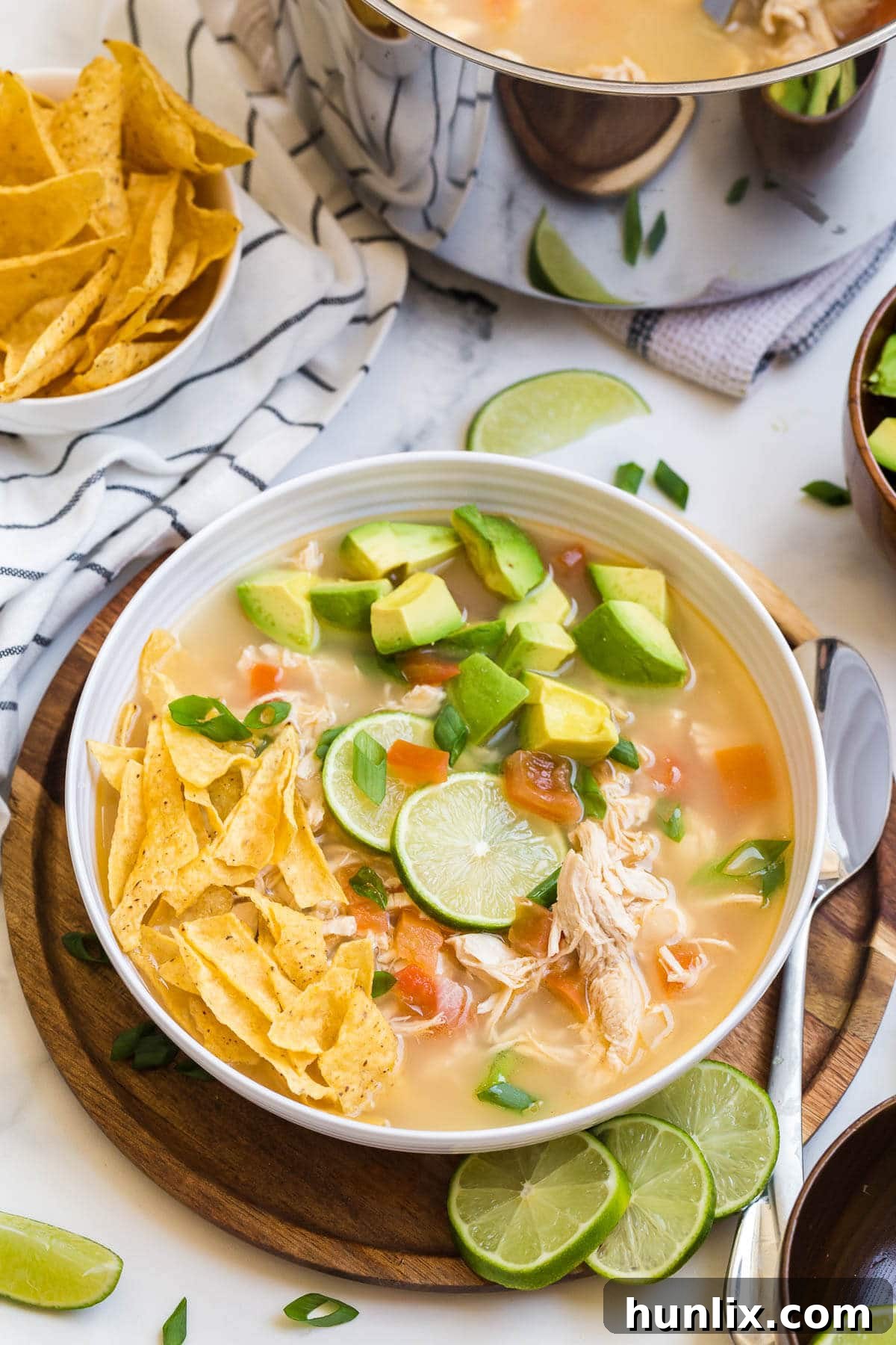A steaming bowl of Chicken and Lime Soup garnished with avocado, tortilla chips, and green onion.