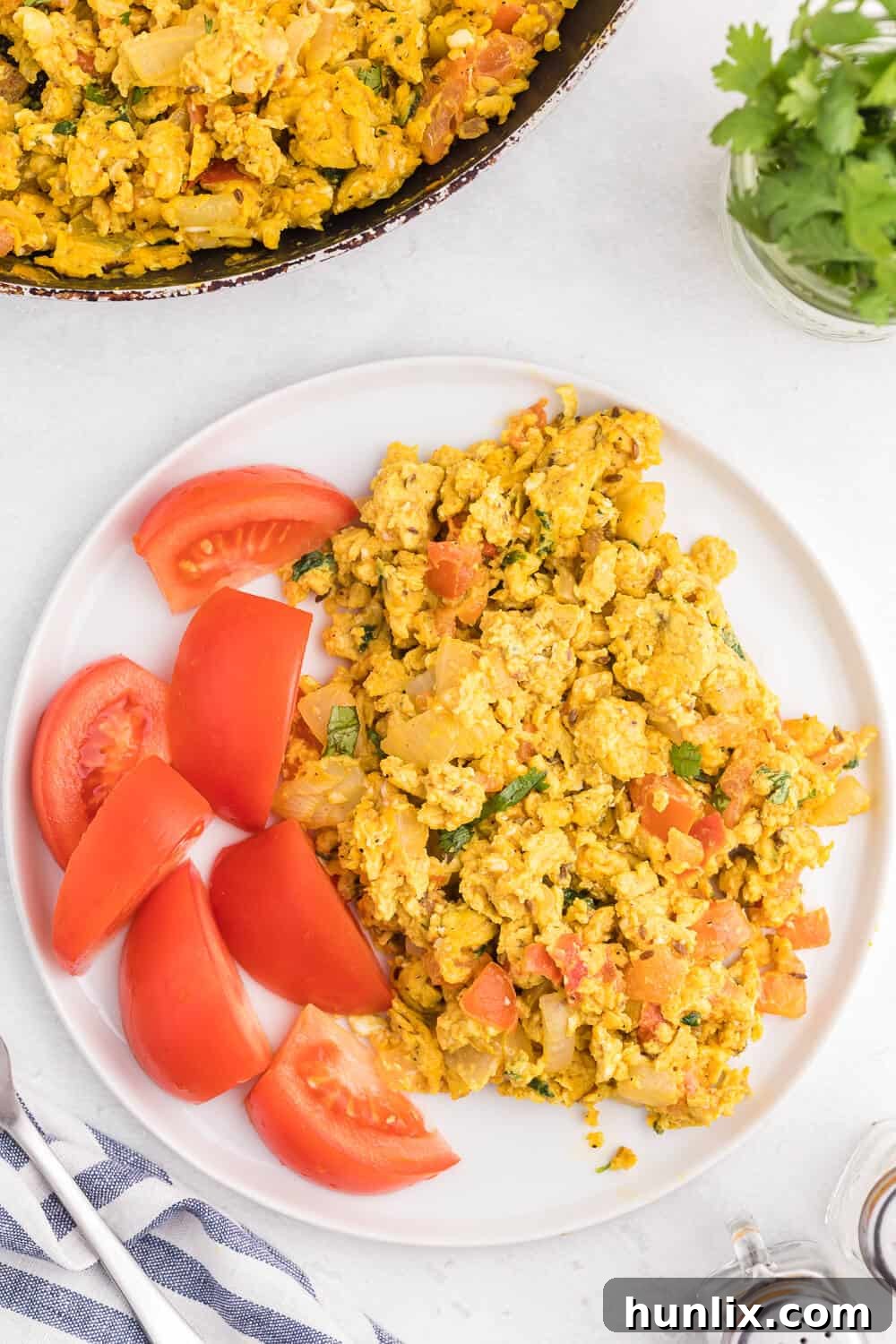 A serving of Indian Scrambled Eggs garnished with fresh cilantro and a tomato wedge, presented in a bowl, ready to be enjoyed.