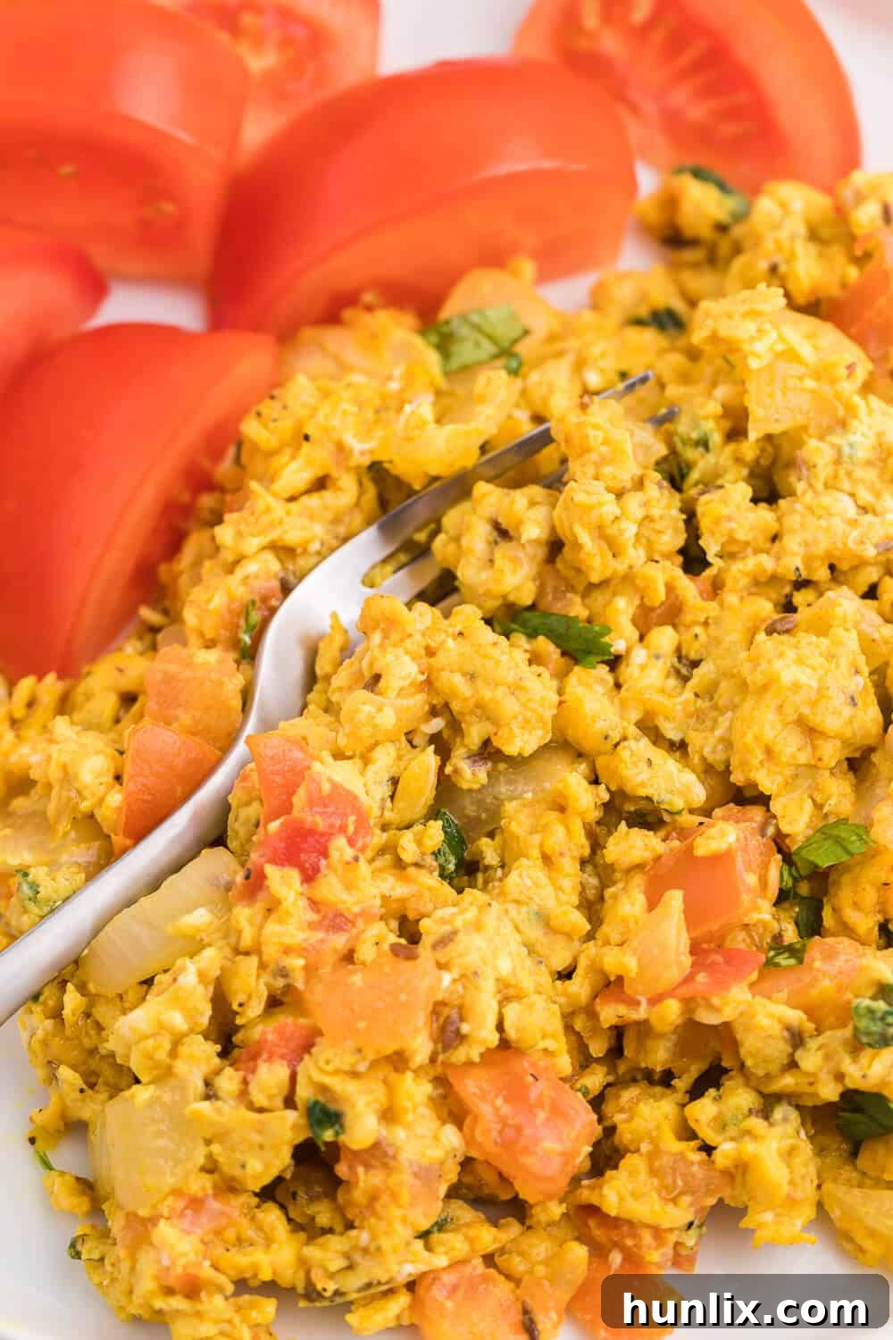 A close-up shot of Indian Scrambled Eggs in a skillet with a spatula, highlighting the soft, creamy texture and vibrant spices.